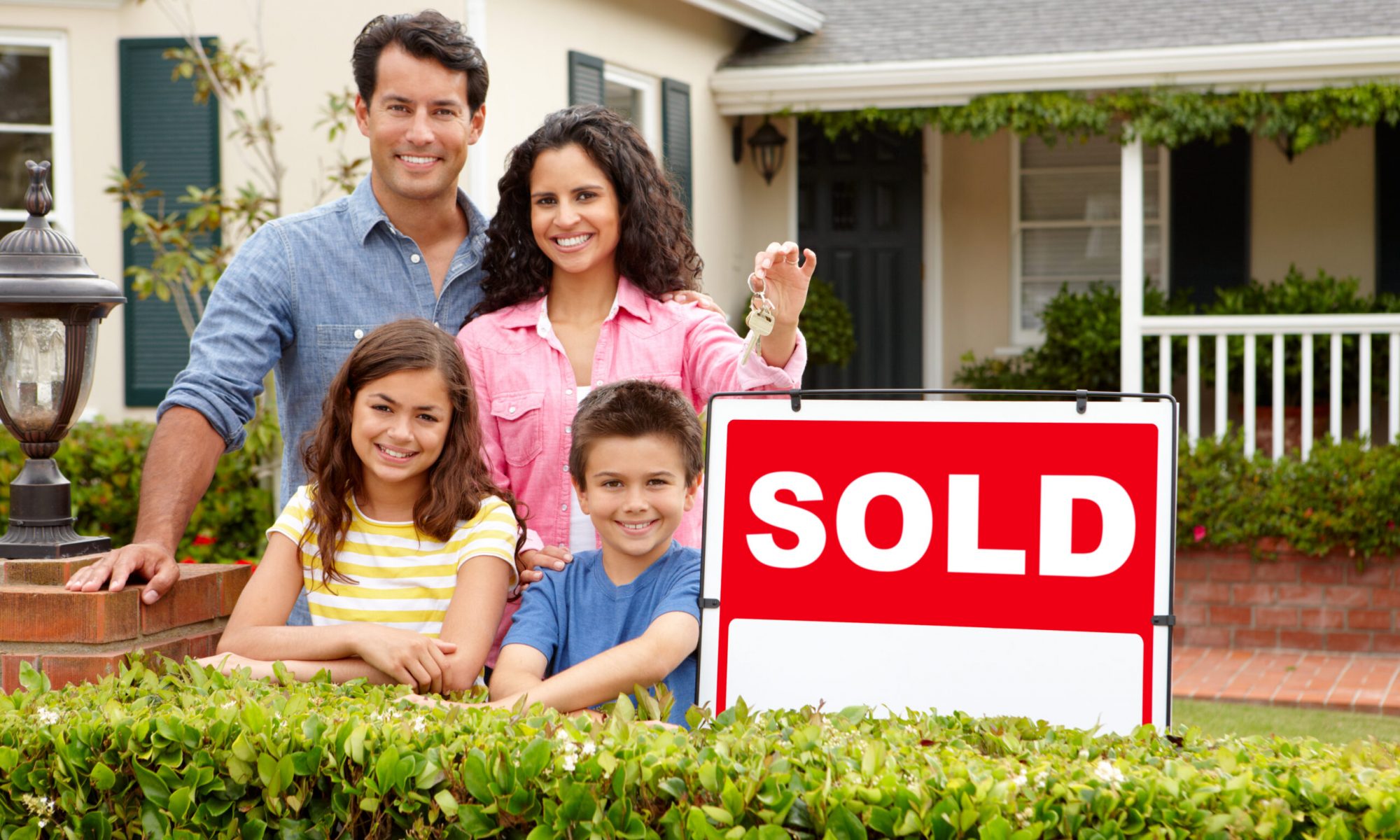 Hispanic family standing outside home smiling with sold sign